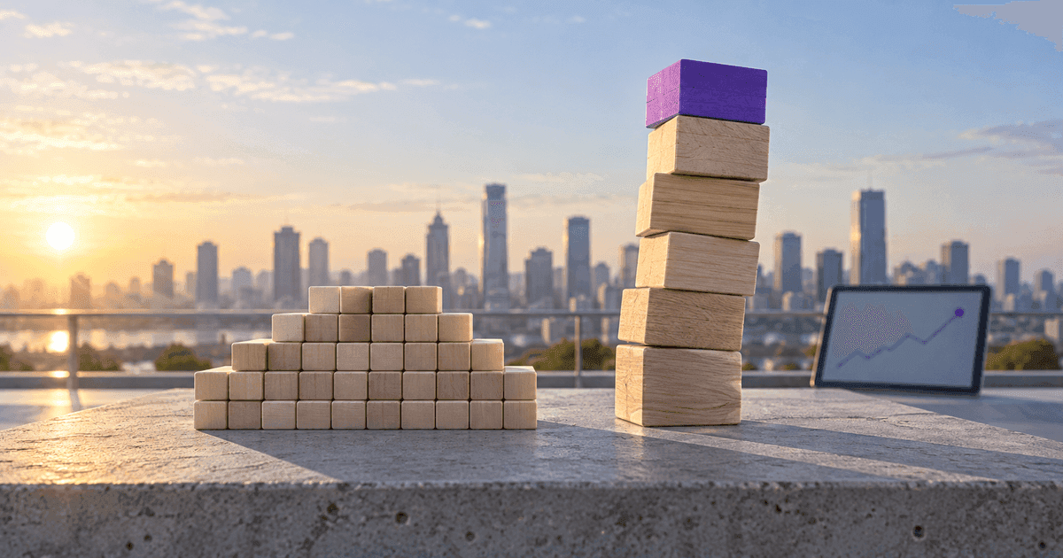Two stacks of wooden blocks on a desk beside a laptop showing a rising chart — a wide, even stack and a taller, narrower one — with one block at the top of the tall stack in violet